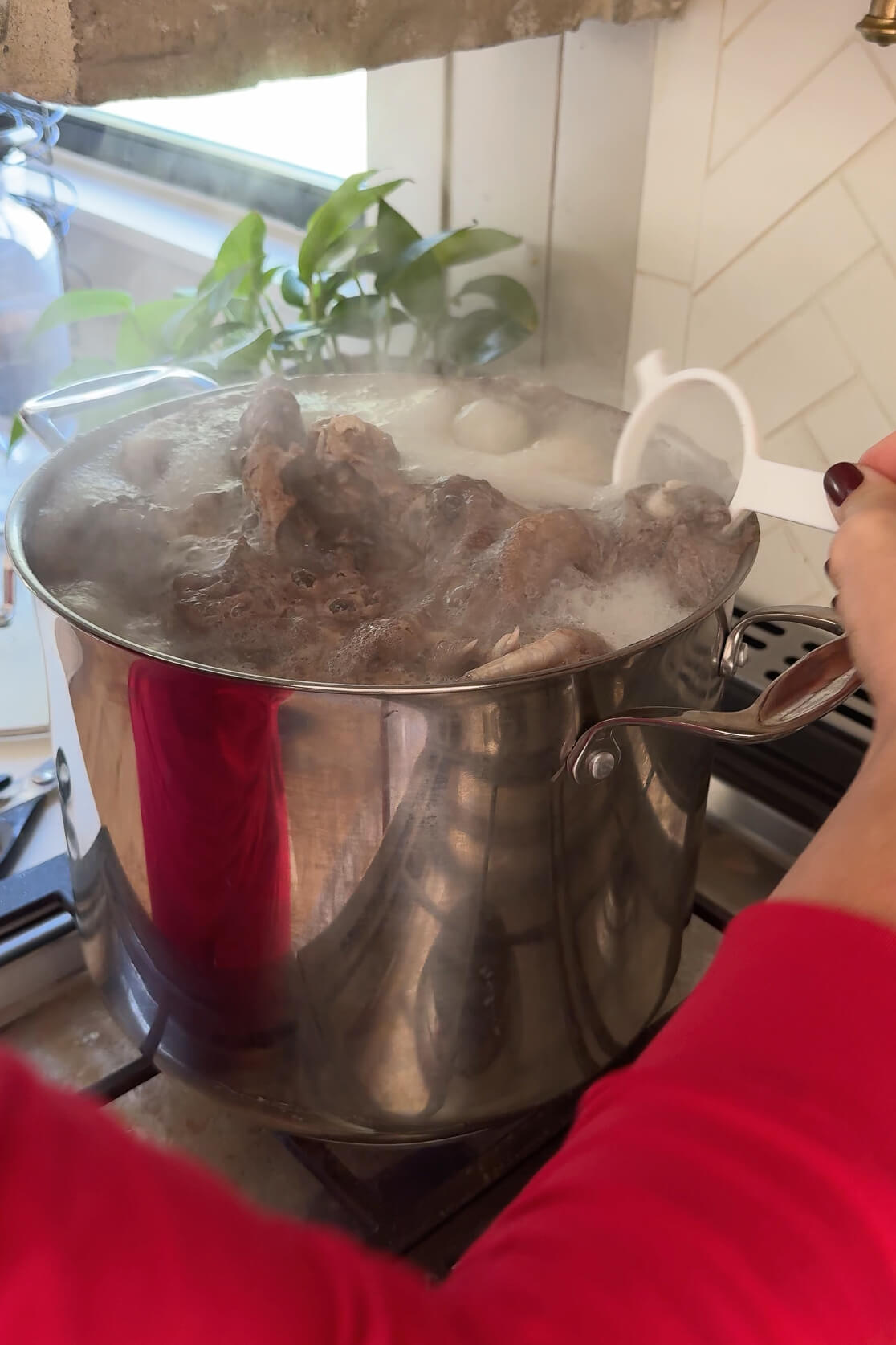 Scooping "scum" off the top of the homemade chicken stock as it cooks.